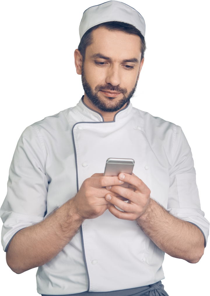 Un chef con uniforme blanco y sombrero está concentrado en su teléfono inteligente, posiblemente revisando las ventas de WhatsApp para perfeccionar sus estrategias culinarias.